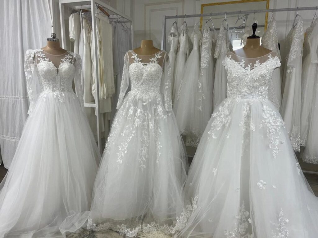 Three white lace wedding dresses displayed on mannequins inside a bridal boutique.