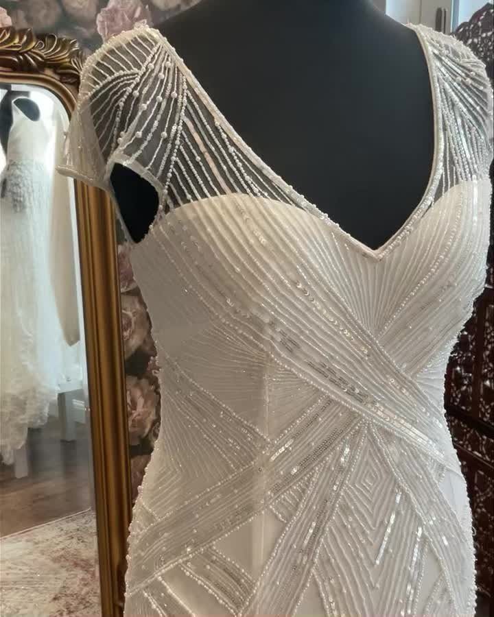 A white wedding dress with silver geometric beadwork displayed on a black mannequin.