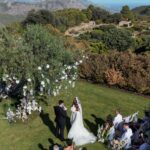 A bride and groom exchange vows during an outdoor wedding ceremony overlooking mountains and the sea.