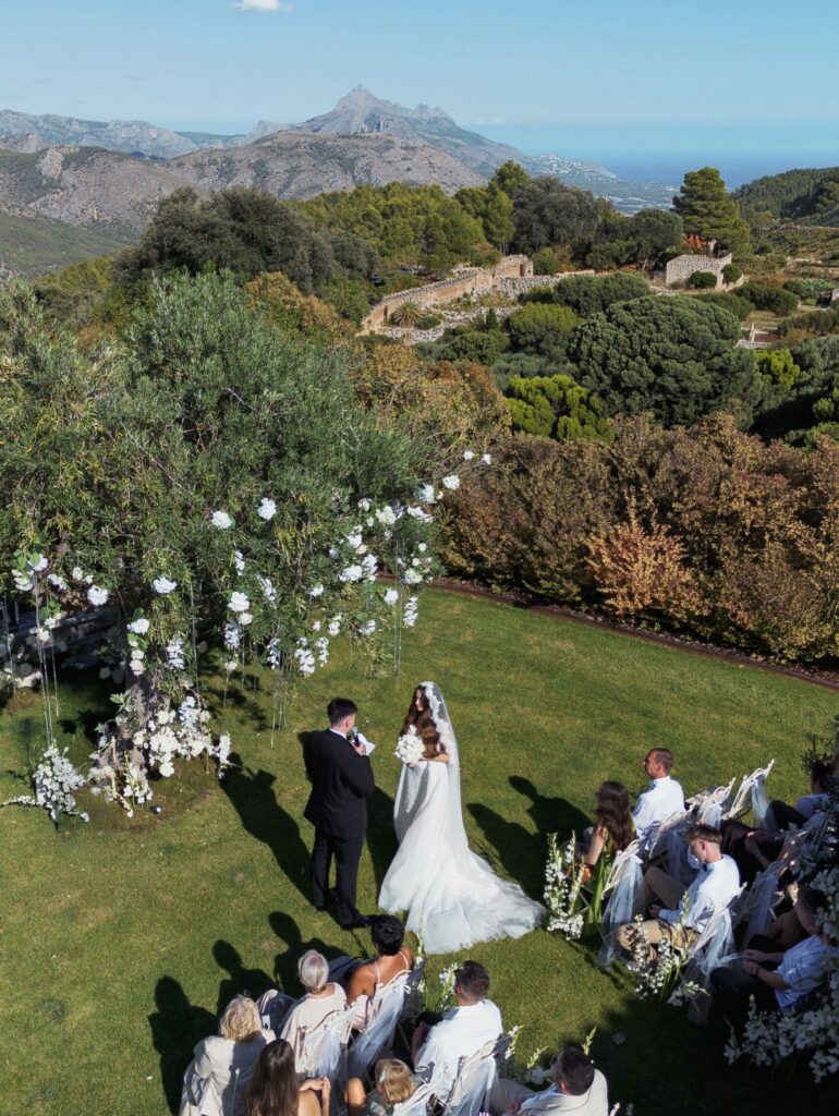 A bride and groom exchange vows during an outdoor wedding ceremony overlooking mountains and the sea.