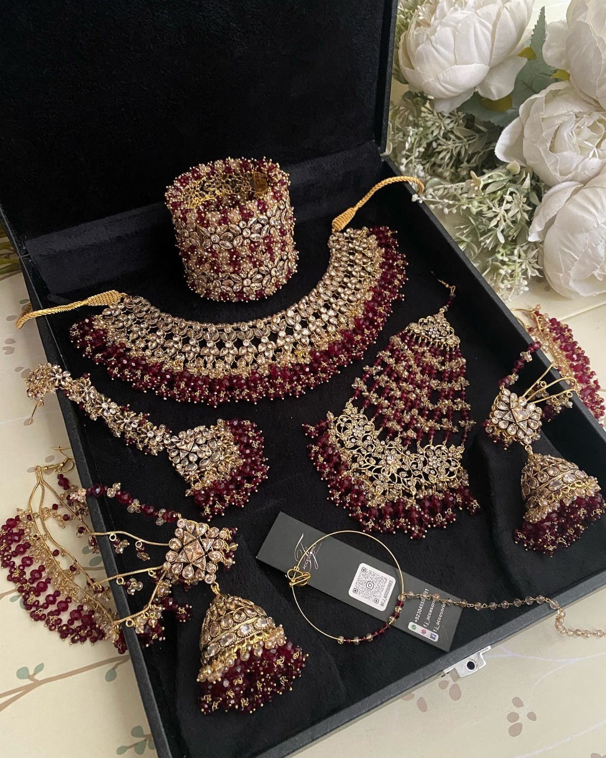 Ornate gold and red beaded Pakistani bridal jewelry set displayed in a black velvet box.