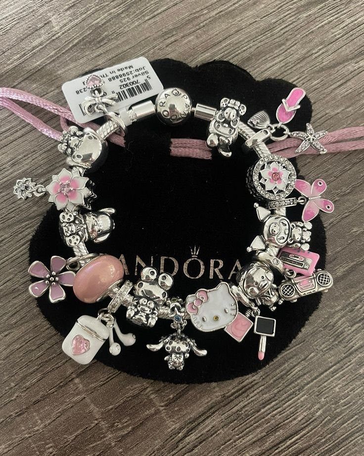 A silver charm bracelet with pink floral and character charms on a black cushion.