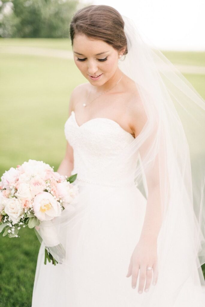 Bride in sweetheart neckline wedding dress wearing a delicate pendant necklace and holding roses.