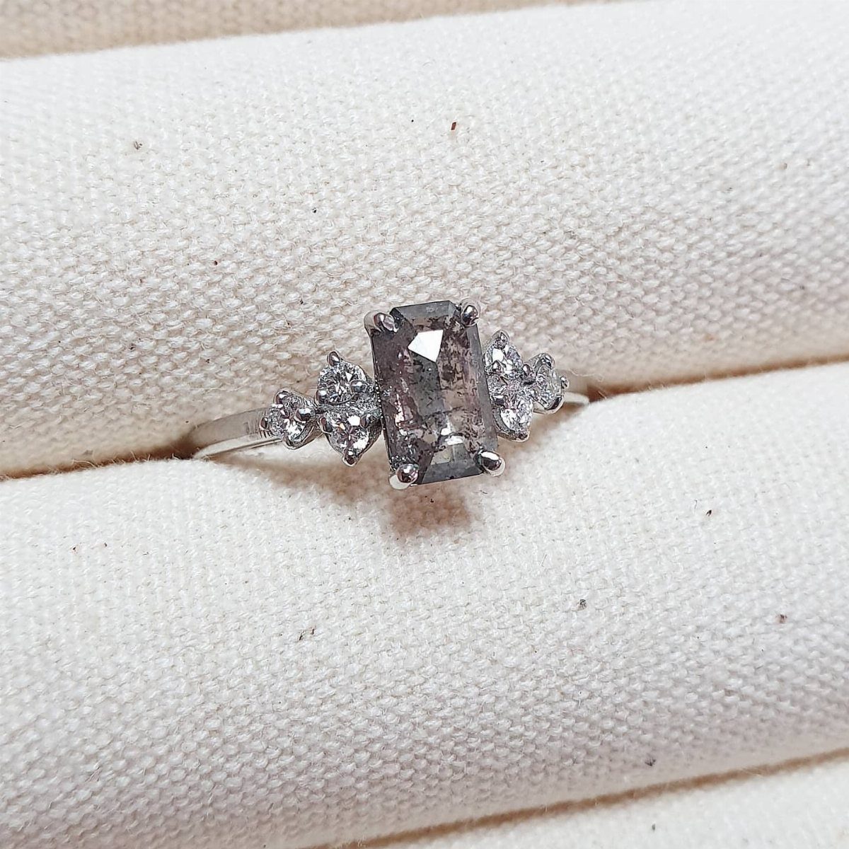 A rectangular salt and pepper diamond ring with small accent stones on white fabric.