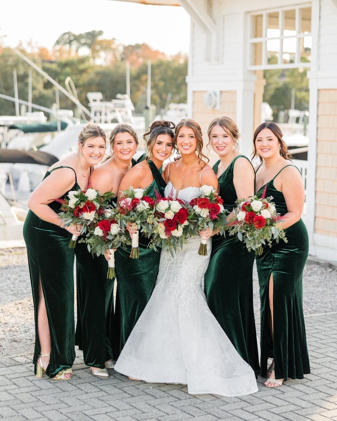 Bridesmaids in dark green velvet dresses holding red and white bouquets standing with a bride.