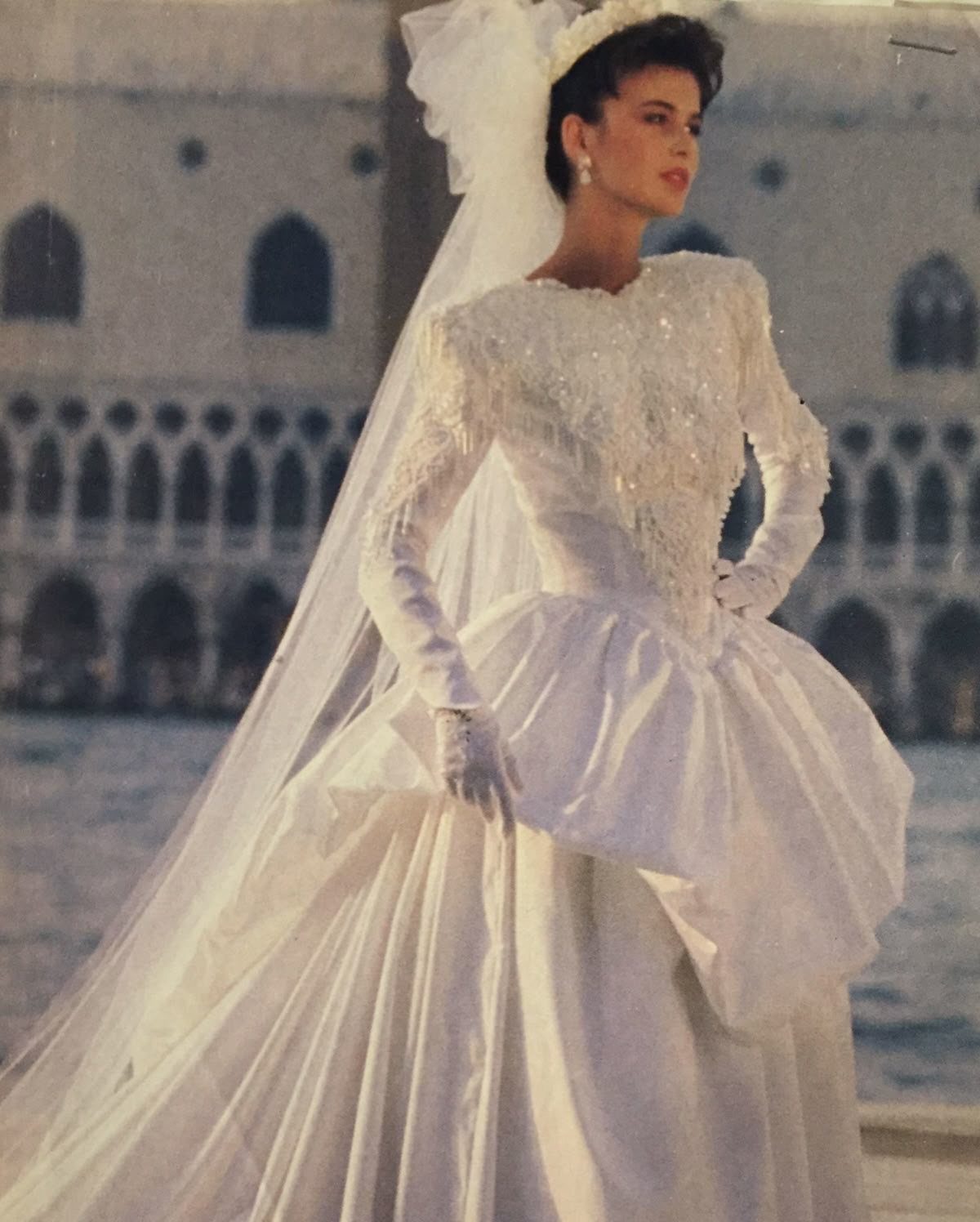 Woman wearing a vintage 90s style white satin wedding dress with beaded bodice and long veil.