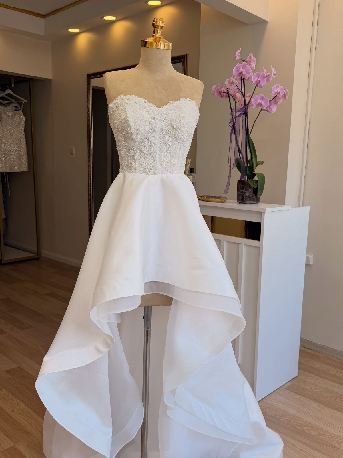 A white strapless wedding dress with a lace bodice and high-low skirt on a mannequin.