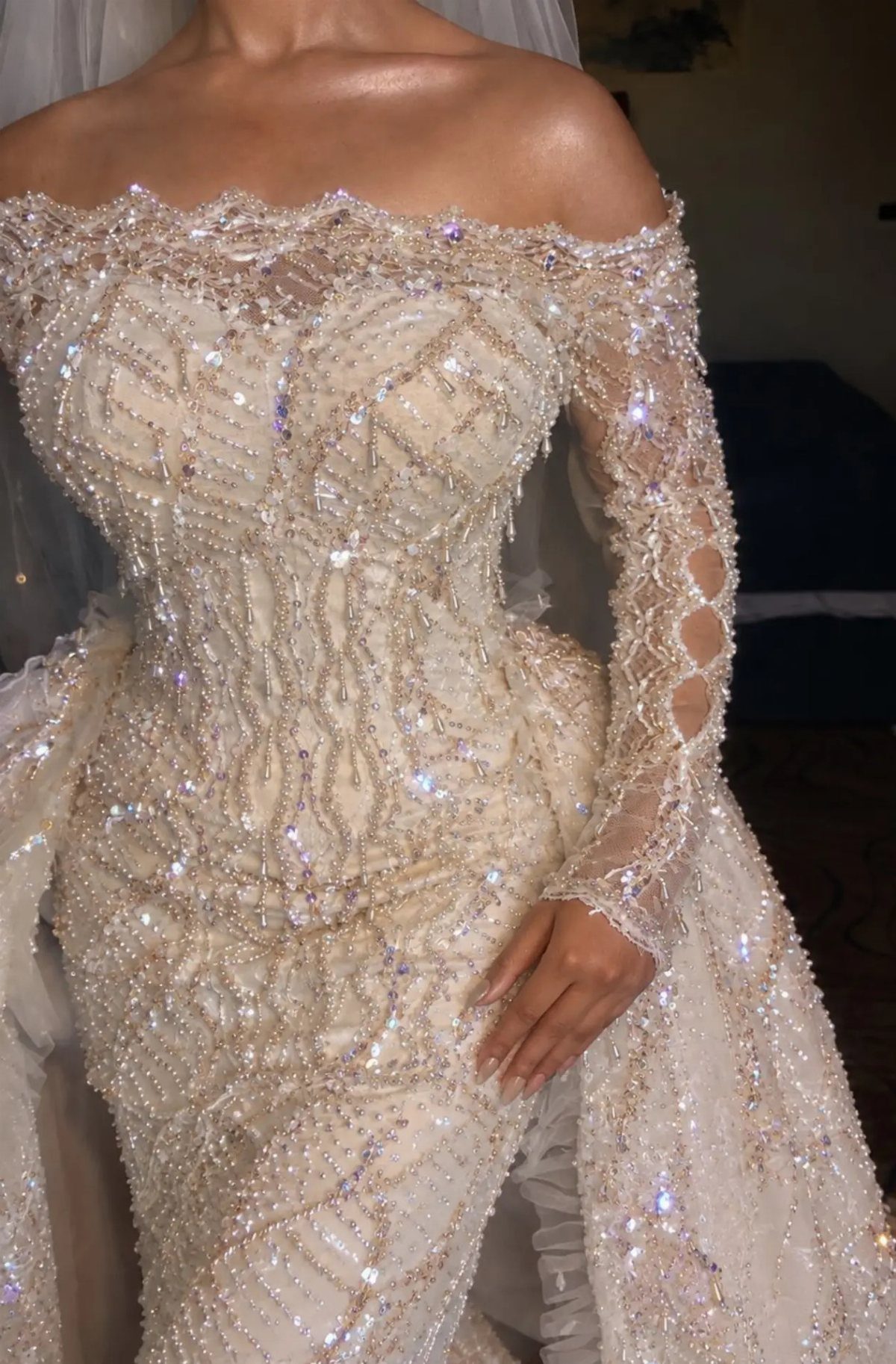 An embellished off-the-shoulder wedding dress featuring intricate gold beadwork, pearls, and shimmering sequins.