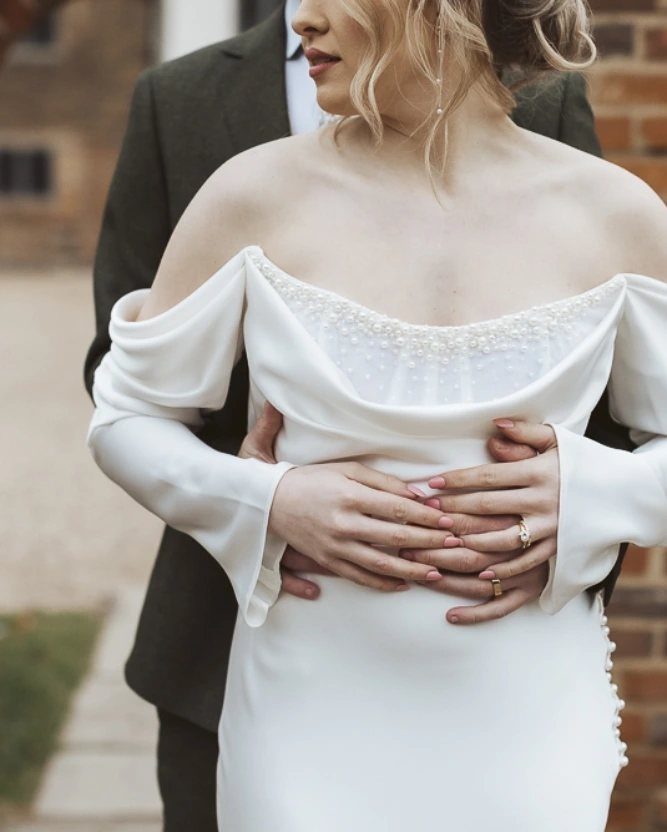 Woman wearing an off-the-shoulder white wedding dress with pearl details on the neckline.
